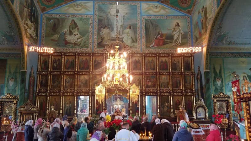 Парафіяни в хустках перед іконостасом із написом «Христос воскресе», біля відчинених царських врат священник