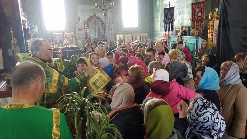 Священник у зелених ризах серед парафіян, які тісно стоять у храмі в теплому одязі й хустках