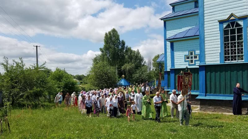 Хресна хода біля храму: чоловіки з хоругвами, священнослужителі в зелених ризах і парафіяни йдуть по траві