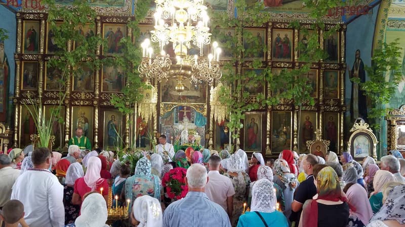 Іконостас прибраний зеленими гілками, біля царських врат священники в зелених ризах, храм повний людей