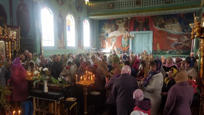 Парафіяни з вербовими гілками й запаленими свічками в храмі, серед них священник у митрі